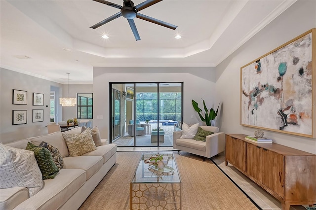 living room with ceiling fan with notable chandelier, a raised ceiling, ornamental molding, and light tile patterned flooring