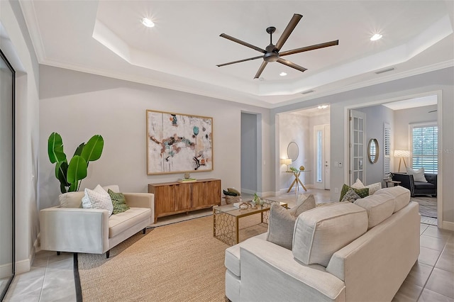 living room featuring ceiling fan, a raised ceiling, light tile patterned floors, and crown molding