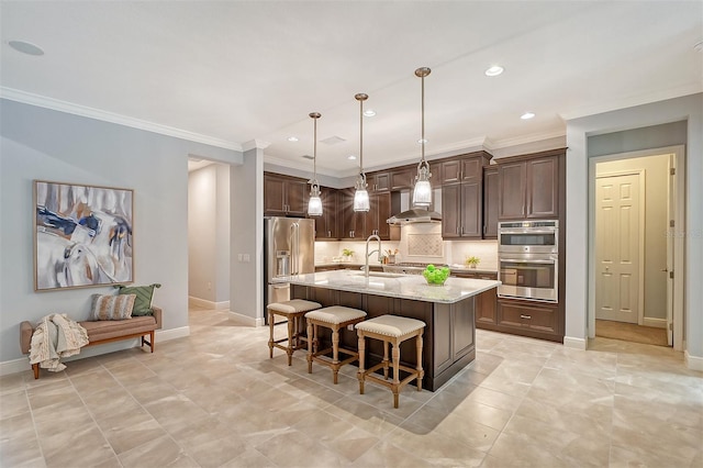 kitchen with a kitchen island with sink, wall chimney range hood, appliances with stainless steel finishes, decorative light fixtures, and light stone counters