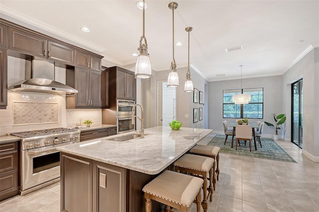 kitchen with sink, stainless steel appliances, range hood, pendant lighting, and a center island with sink