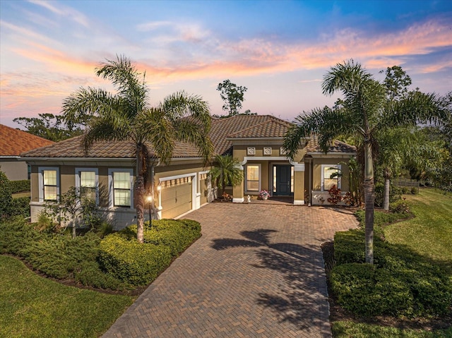 mediterranean / spanish house featuring a tiled roof, decorative driveway, a lawn, and stucco siding