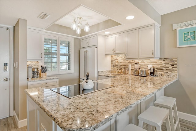 kitchen with sink, high end refrigerator, white cabinets, kitchen peninsula, and black electric cooktop