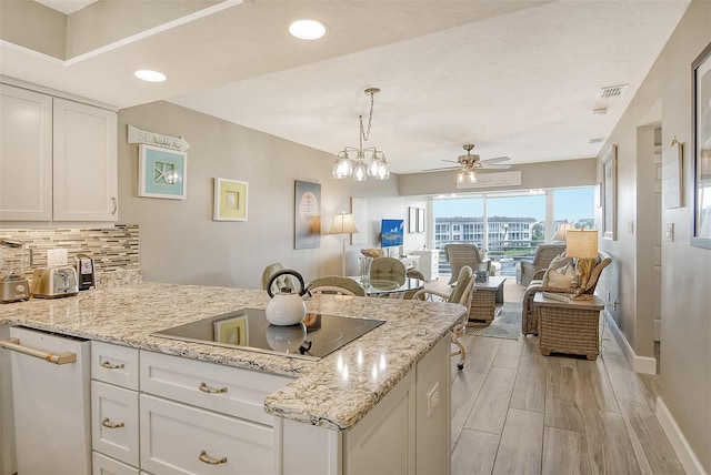 kitchen featuring black electric cooktop, light stone counters, ceiling fan with notable chandelier, and white cabinets