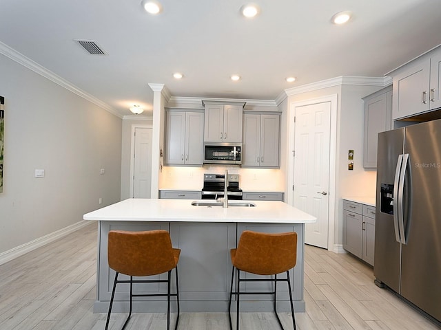 kitchen with gray cabinets, a kitchen island with sink, appliances with stainless steel finishes, and light hardwood / wood-style flooring