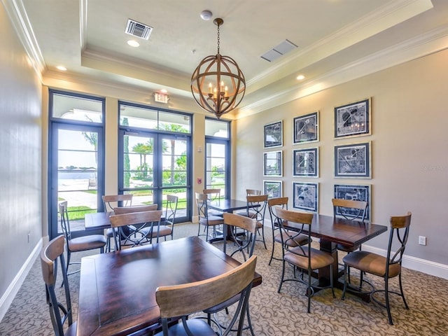 carpeted dining space with a tray ceiling, french doors, ornamental molding, and a notable chandelier