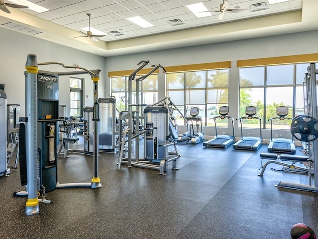 gym with a drop ceiling, ceiling fan, and a towering ceiling