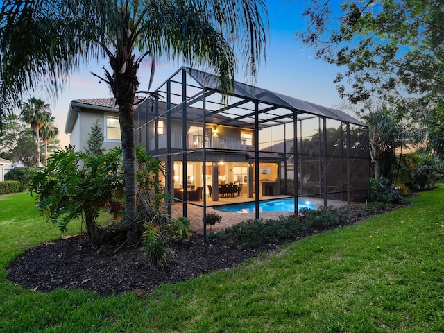 pool at dusk with glass enclosure, a yard, and a patio