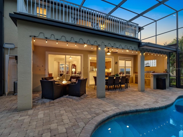 back house at dusk with a lanai, a balcony, an outdoor hangout area, and a patio