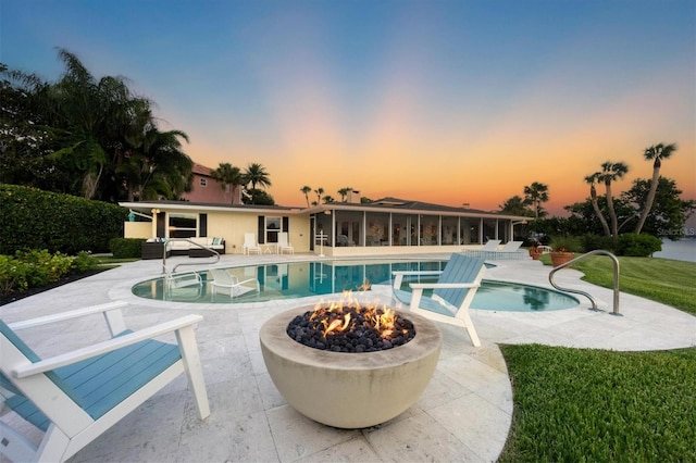 pool at dusk featuring an outdoor living space with a fire pit, a sunroom, and a patio