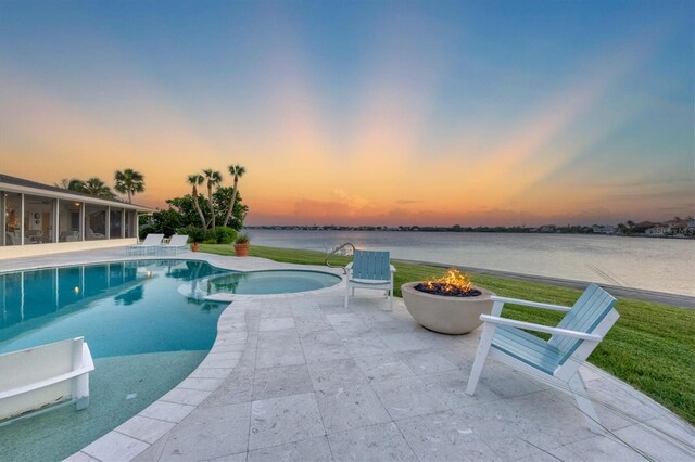 pool at dusk featuring a fire pit, a sunroom, a water view, an in ground hot tub, and a patio