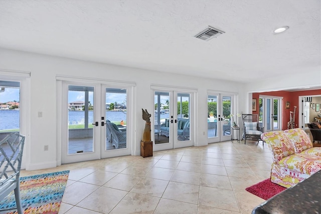 living room with light tile patterned floors, a water view, and french doors