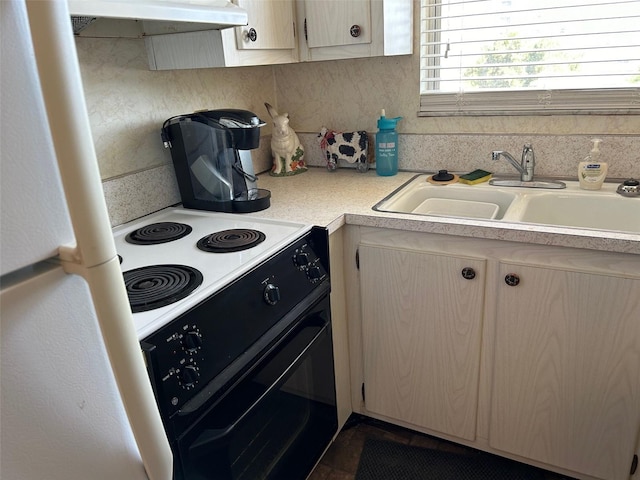 kitchen featuring under cabinet range hood, a sink, light countertops, freestanding refrigerator, and black electric range oven