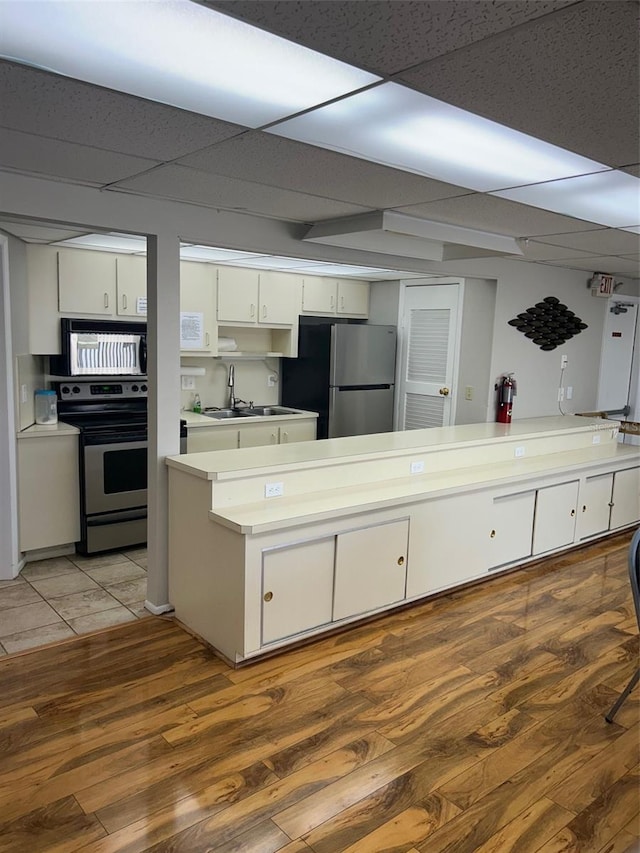 kitchen featuring stainless steel appliances, a drop ceiling, white cabinetry, wood-type flooring, and sink