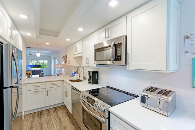 kitchen featuring white cabinetry, sink, stainless steel appliances, light hardwood / wood-style flooring, and kitchen peninsula