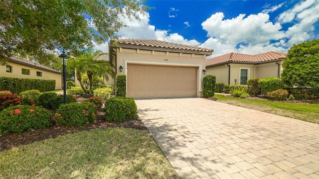 mediterranean / spanish house with a garage, stucco siding, decorative driveway, and a tiled roof