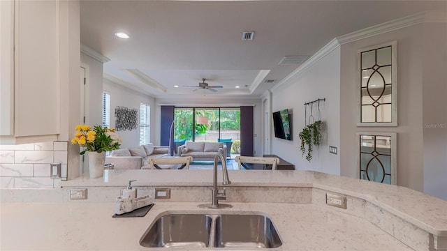 kitchen featuring sink, crown molding, ceiling fan, a tray ceiling, and light stone counters