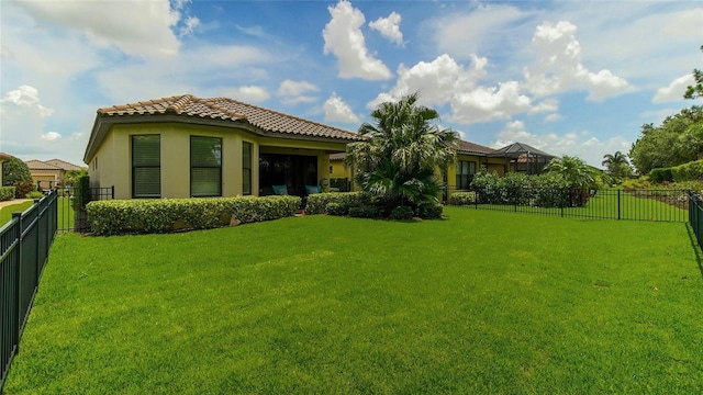 rear view of house featuring a tile roof, a fenced backyard, a yard, and stucco siding