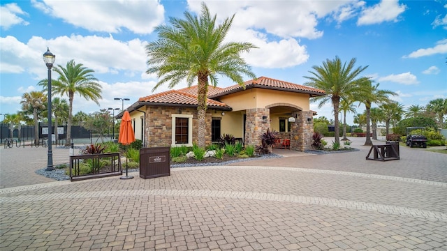 view of front of house featuring stone siding, a tiled roof, fence, and stucco siding