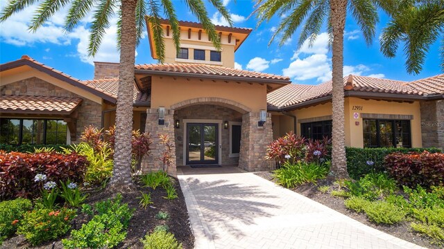 view of exterior entry with stone siding, french doors, a tile roof, and stucco siding