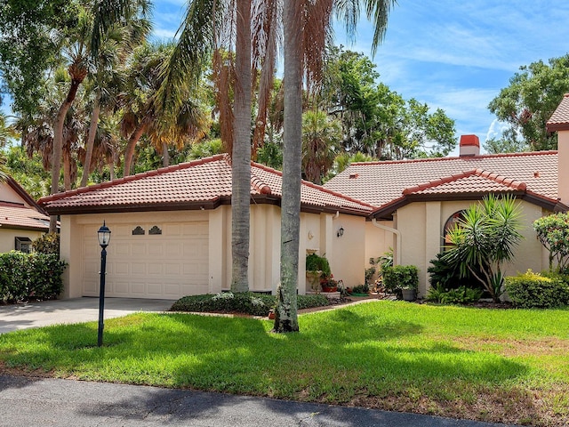 mediterranean / spanish-style home featuring a chimney, a tiled roof, an attached garage, a front yard, and stucco siding