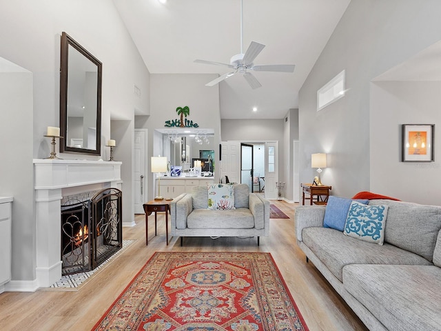 living area with light wood finished floors, baseboards, a ceiling fan, a fireplace with flush hearth, and high vaulted ceiling