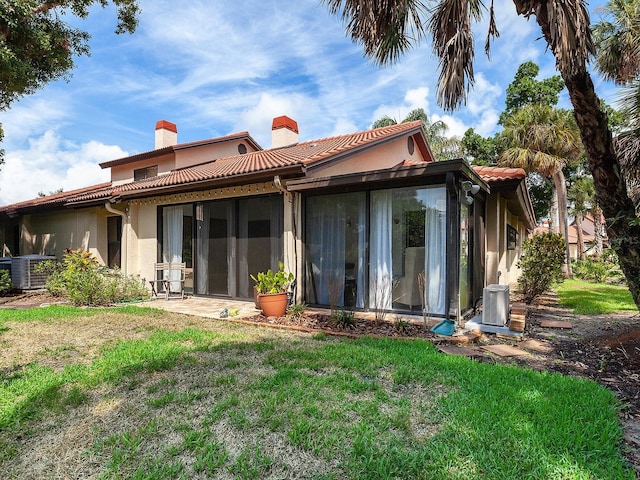 rear view of house featuring a tiled roof, a chimney, cooling unit, and a yard