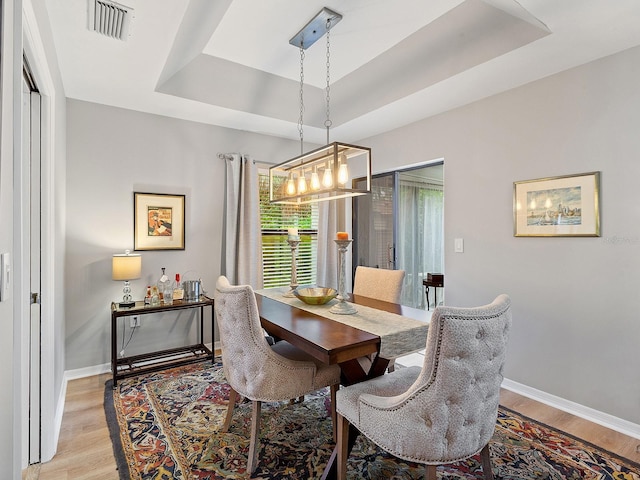 dining space with light wood finished floors, a tray ceiling, visible vents, and baseboards