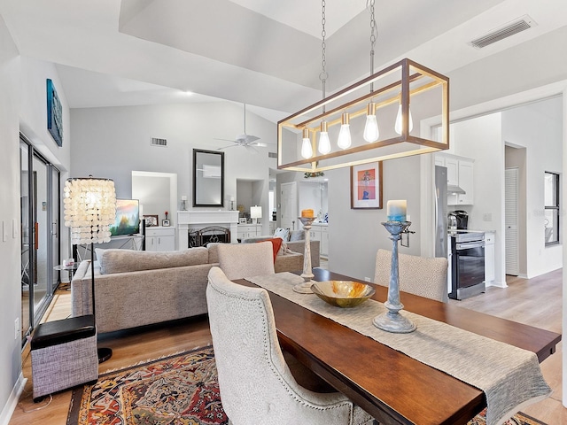 dining space with ceiling fan, high vaulted ceiling, and light hardwood / wood-style flooring