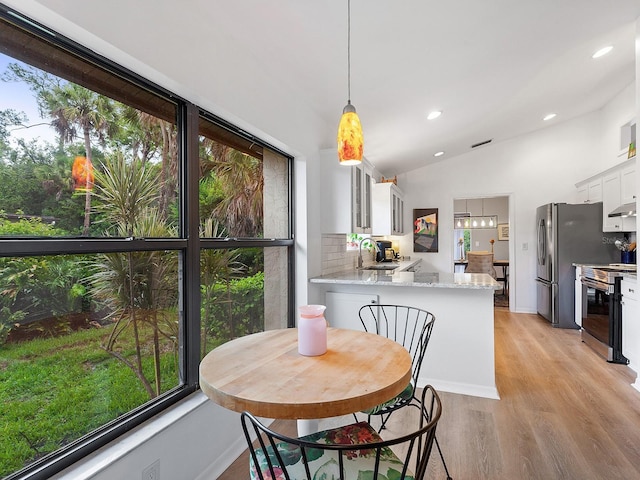 dining space with sink, light hardwood / wood-style flooring, and vaulted ceiling