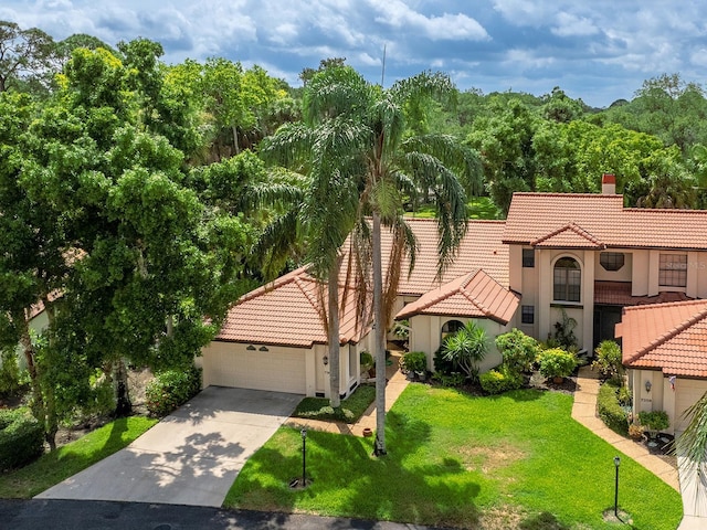 mediterranean / spanish home featuring concrete driveway, a chimney, a tiled roof, a front lawn, and stucco siding