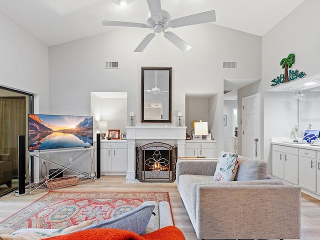 living room with light wood finished floors, a lit fireplace, visible vents, and ceiling fan