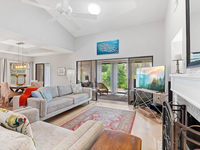 living area with light wood finished floors, a fireplace, a raised ceiling, and ceiling fan with notable chandelier