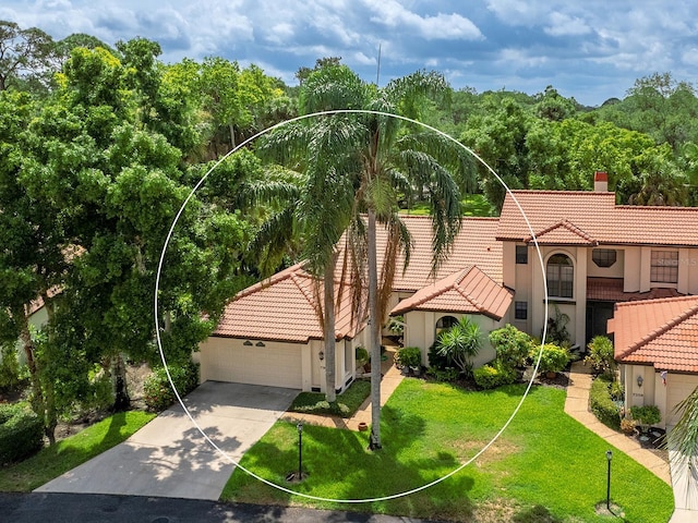 mediterranean / spanish house featuring a tile roof, a chimney, stucco siding, a front yard, and driveway