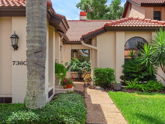 property entrance featuring a tiled roof, a chimney, and stucco siding