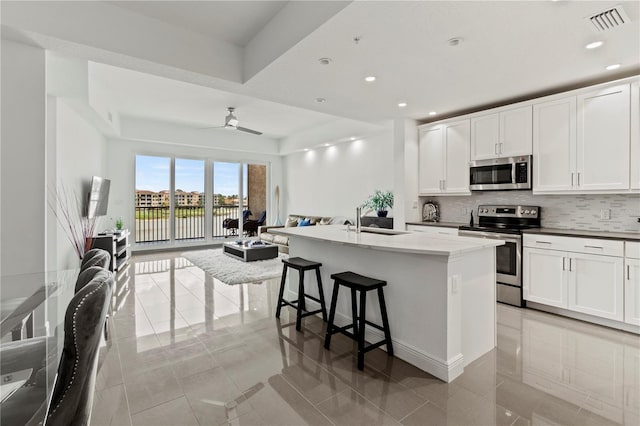 kitchen featuring white cabinets, ceiling fan, an island with sink, and appliances with stainless steel finishes