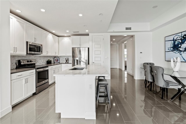 kitchen with white cabinets, stainless steel appliances, a kitchen bar, and a center island with sink