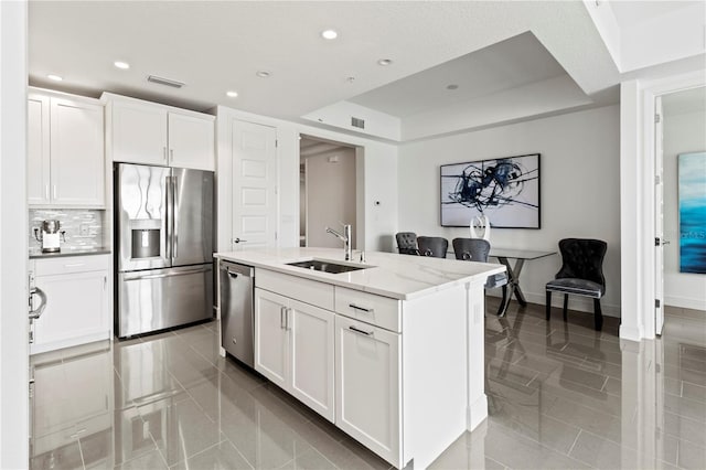 kitchen with sink, white cabinets, an island with sink, light stone countertops, and appliances with stainless steel finishes