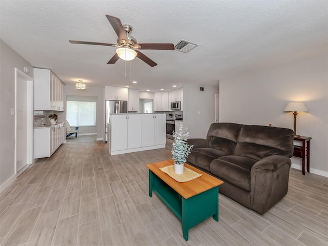 living room featuring a textured ceiling, light wood-type flooring, and ceiling fan