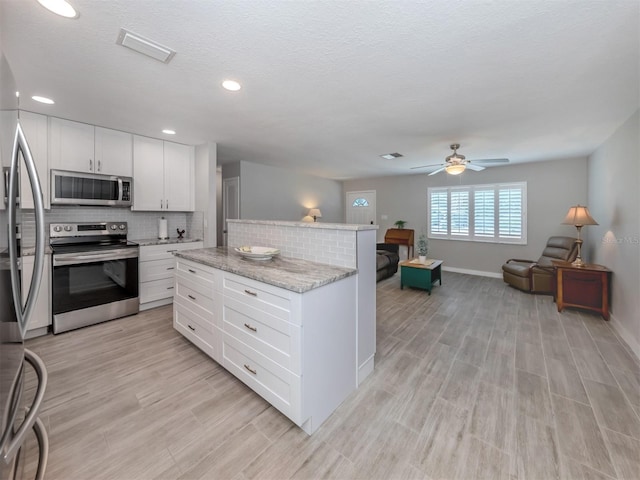 kitchen featuring light stone countertops, appliances with stainless steel finishes, backsplash, ceiling fan, and white cabinets