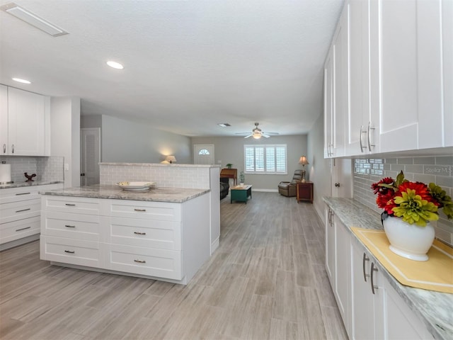 kitchen featuring backsplash, white cabinetry, ceiling fan, and light stone countertops