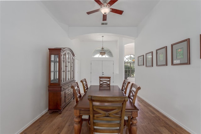 dining area with ceiling fan, wood-type flooring, and a towering ceiling