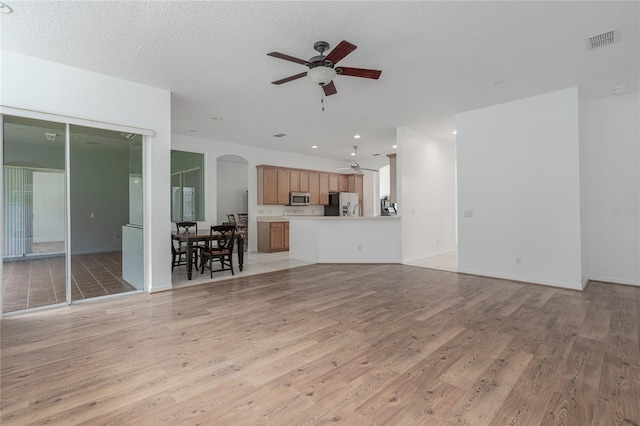 unfurnished living room with a textured ceiling, light hardwood / wood-style flooring, and ceiling fan