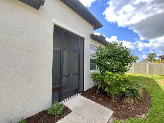 entrance to property with stucco siding, a yard, and fence