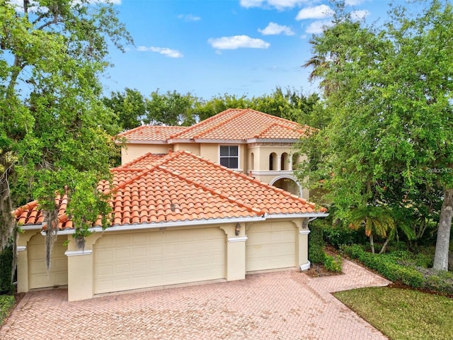 mediterranean / spanish house featuring a garage, driveway, a tile roof, and stucco siding