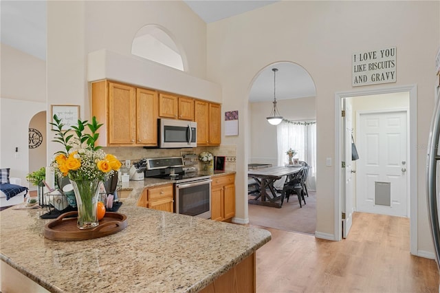 kitchen with hanging light fixtures, light stone counters, a high ceiling, and appliances with stainless steel finishes