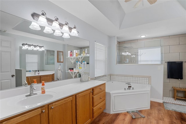 bathroom with vanity, a raised ceiling, hardwood / wood-style flooring, ceiling fan, and independent shower and bath