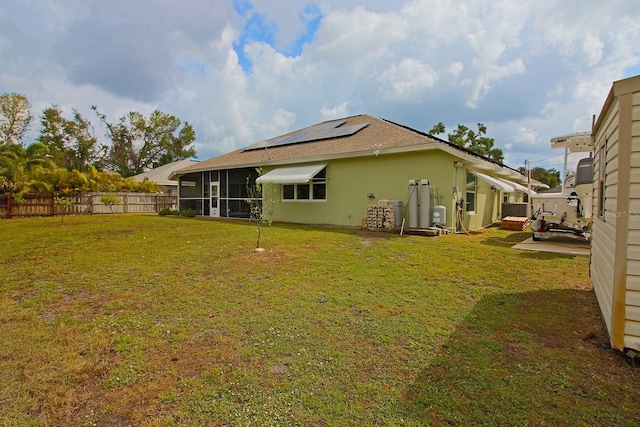 rear view of property featuring solar panels, central air condition unit, and a lawn