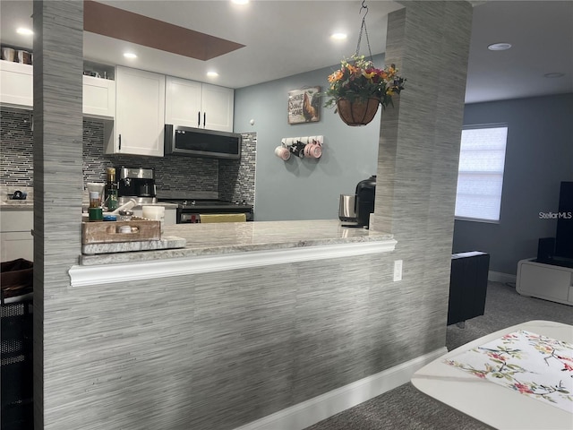 kitchen with white cabinetry, black stove, light stone countertops, kitchen peninsula, and decorative backsplash