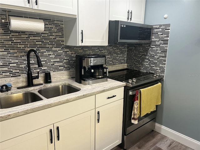 kitchen featuring sink, hardwood / wood-style floors, stainless steel appliances, light stone countertops, and decorative backsplash