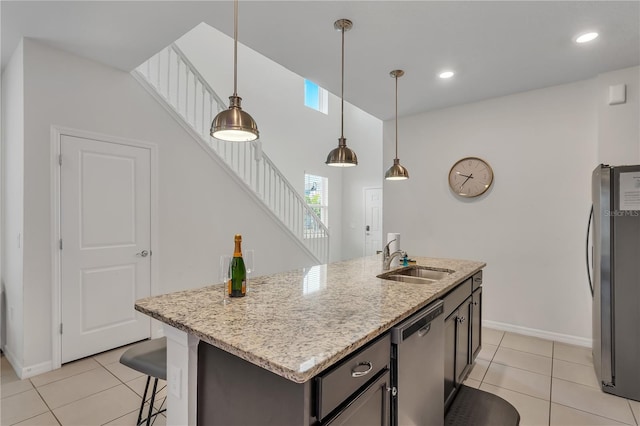 kitchen featuring a kitchen island with sink, sink, light tile patterned floors, decorative light fixtures, and stainless steel appliances